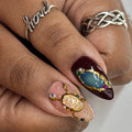 Hand with luxury press-on nails featuring gemstone accents and gold detailing