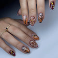 Hand with almond-shaped press-on nails featuring monarch butterfly wing designs, amber ombre, and 3D floral art.