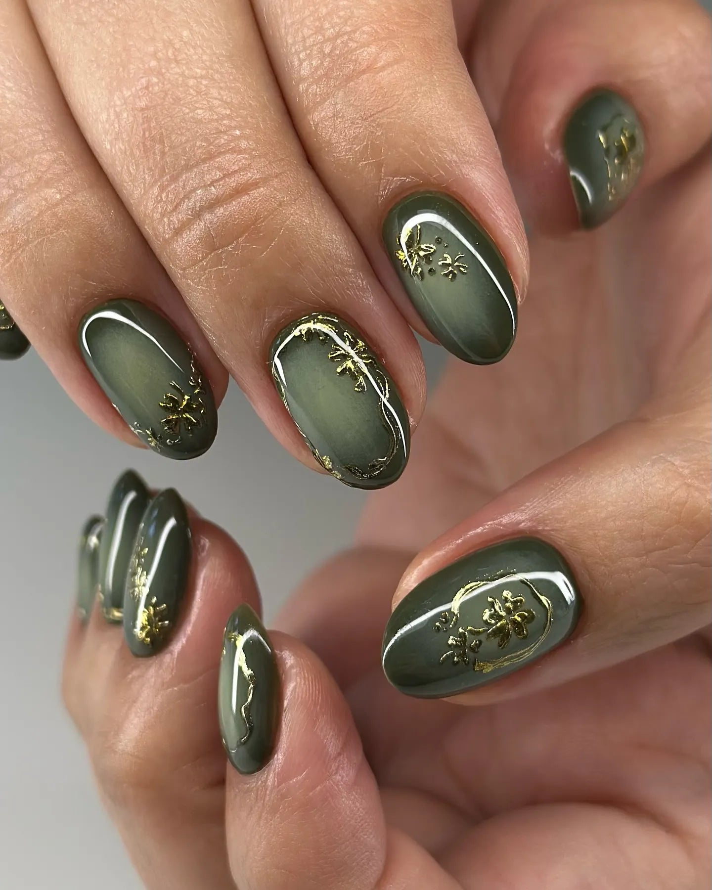 Hand with handmade olive green press-on nails featuring gold botanical accents