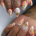 Handmade press-on nails with neon sunset colors, gold swirl accents, white designs, and crystal gems