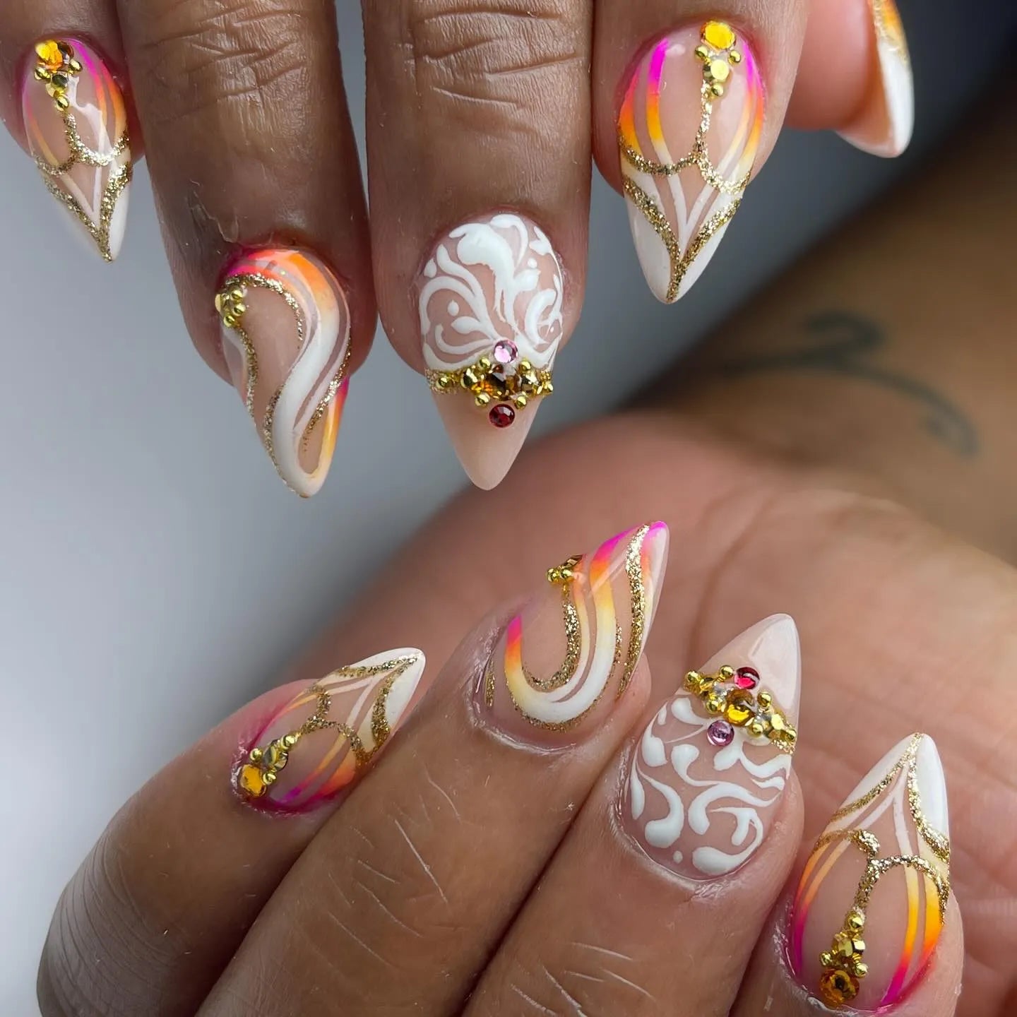 Handmade press-on nails with neon sunset colors, gold swirl accents, white designs, and crystal gems