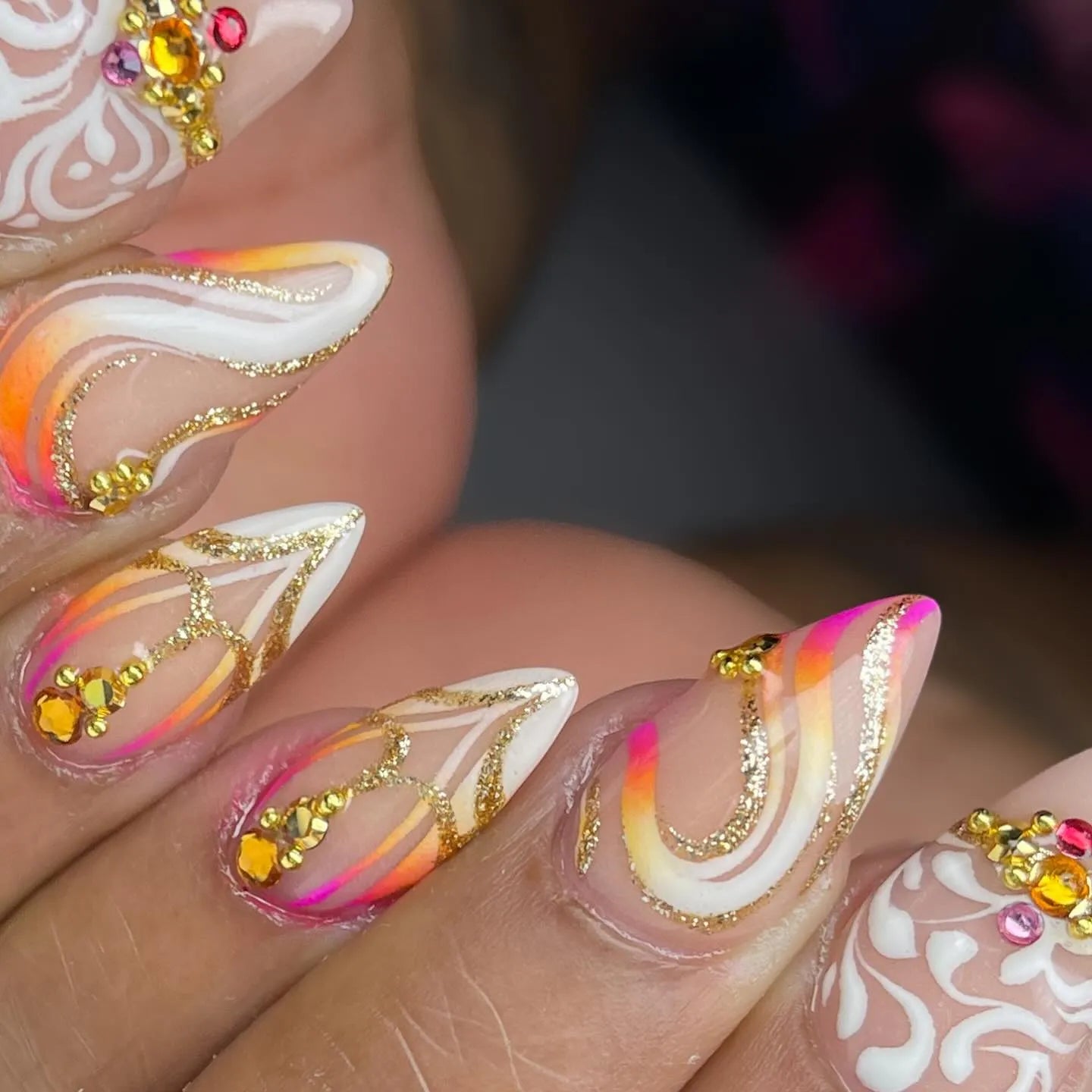 Handmade press-on nails with sunset gradient, gold swirls, white accents, and crystal gems