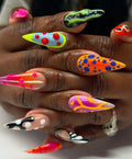 Hand displaying handmade press-on stiletto nails with neon abstract 3D patterns and textures.