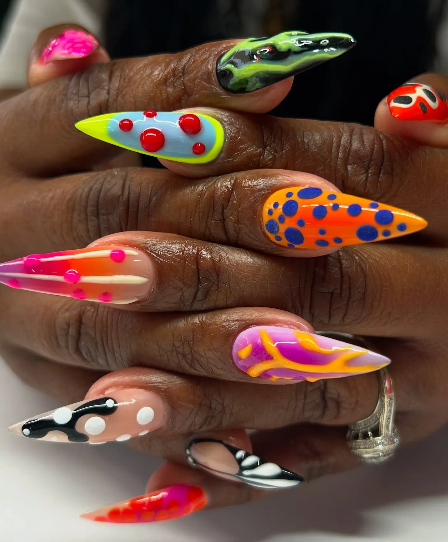 Hand displaying handmade press-on stiletto nails with neon abstract 3D patterns and textures.