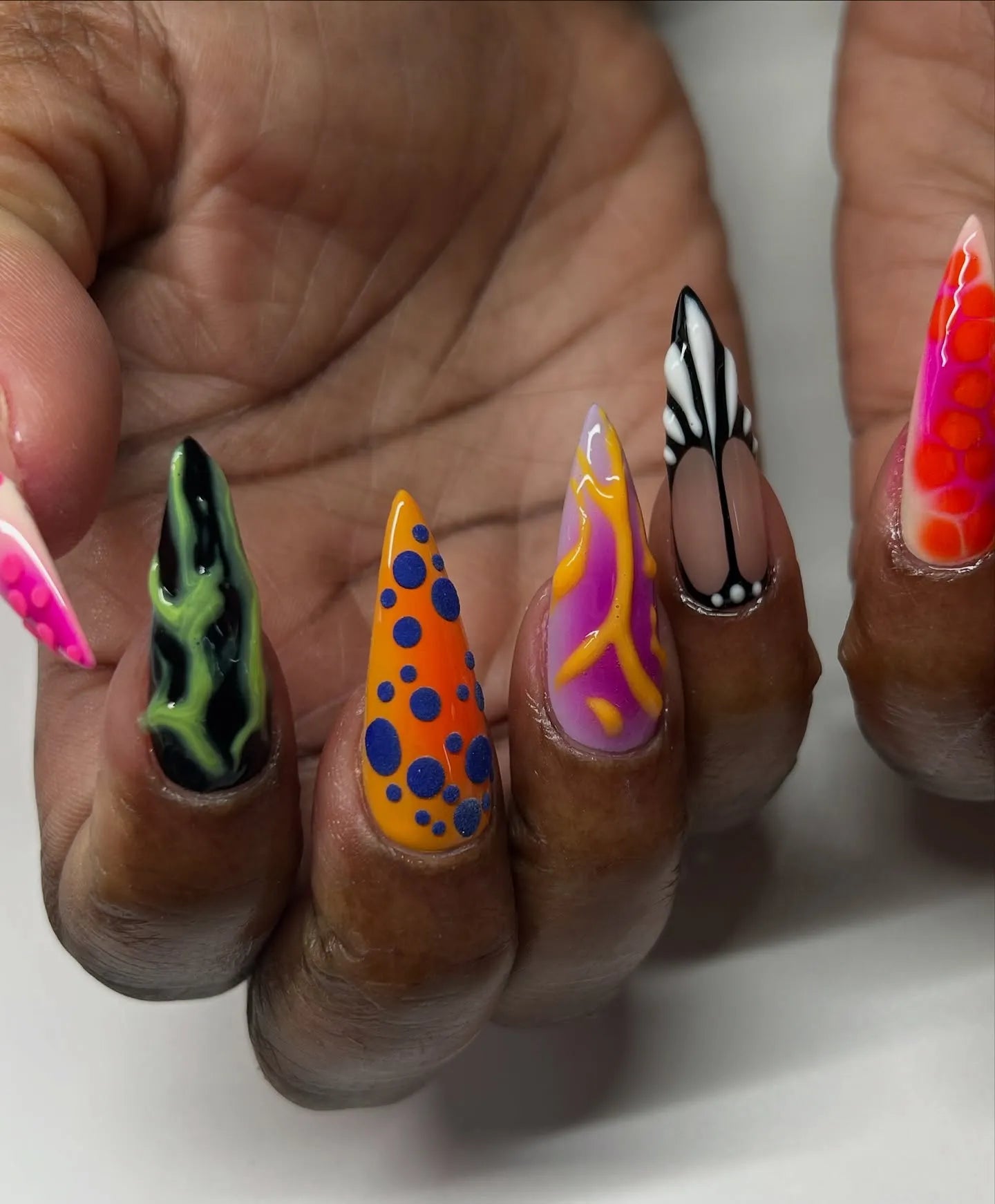 Hand with long stiletto press-on nails in vibrant abstract neon frog pattern designs