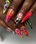 Hand wearing long stiletto press-on nails with bright, abstract 3D neon frog and pattern designs.