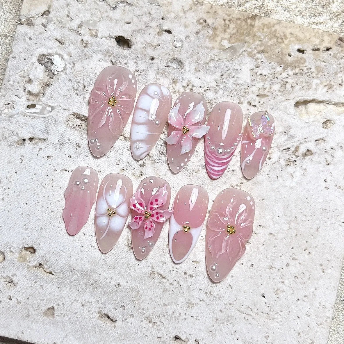 Handmade nude pink press-on nails with 3D petal flowers, pearls, and butterfly accents.