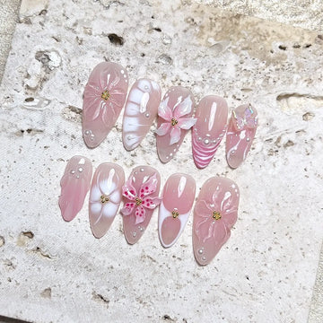Handmade nude pink press-on nails with 3D petal flowers, pearls, and butterfly accents.