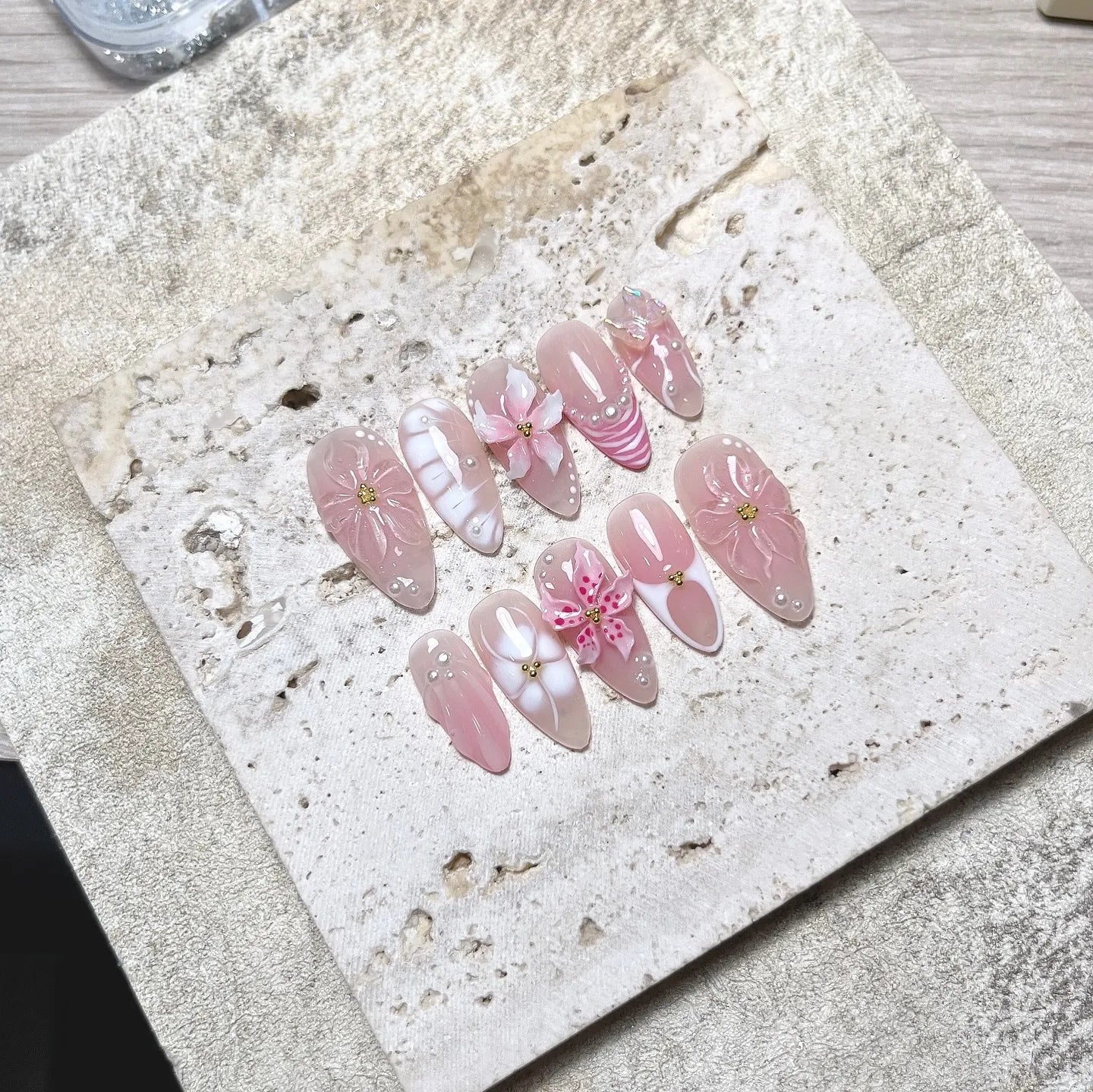 Handmade nude pink 3D petal flower and pearl butterfly press-on nails on textured tray.