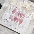 Handmade nude pink press-on nails with 3D flower petals, pearls, and butterfly accents.