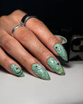 Hand with green nature-themed press-on nails featuring ladybugs and caterpillar art.