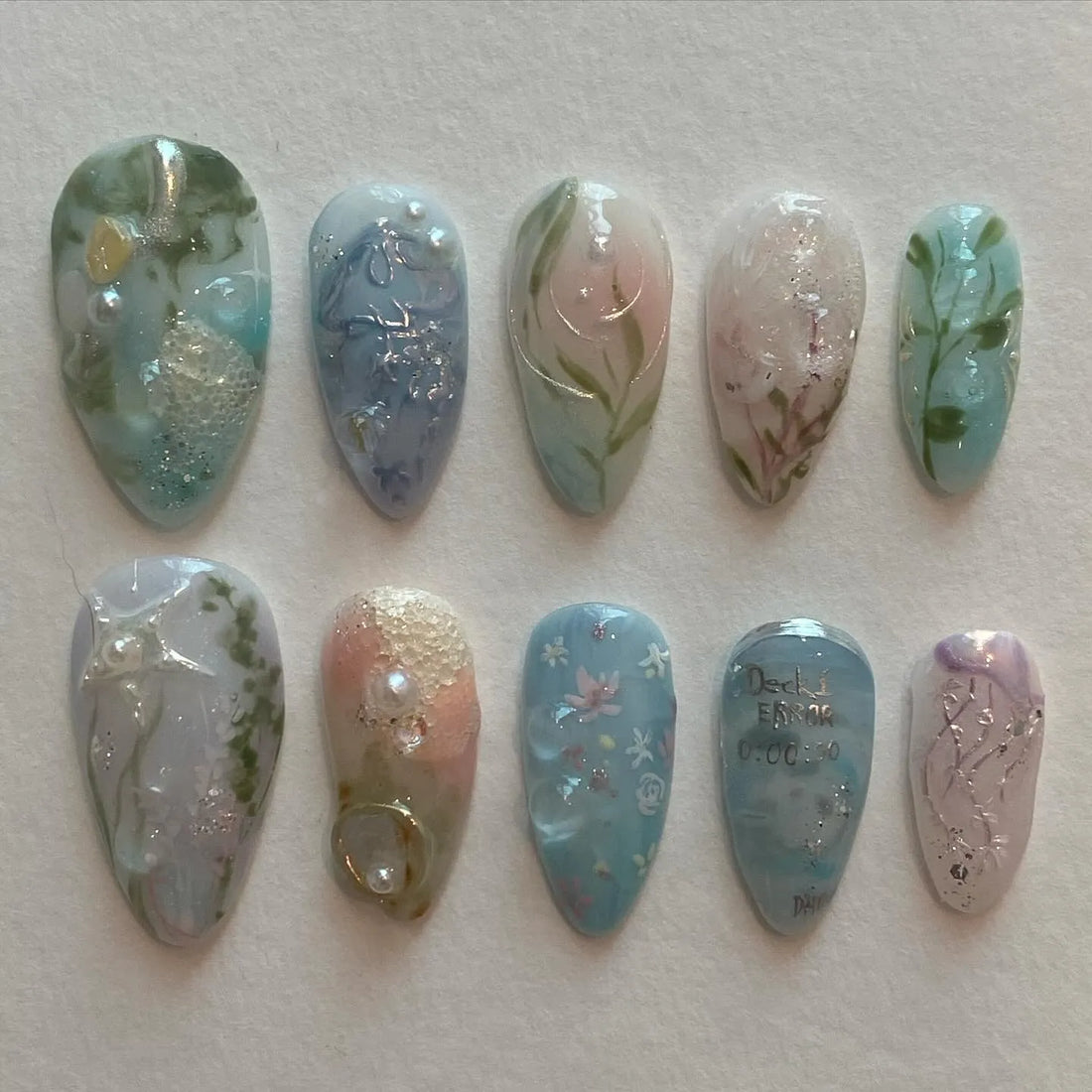 Handmade pale blue ocean-themed press-on nails with jellyfish, water lily, and silver accents.