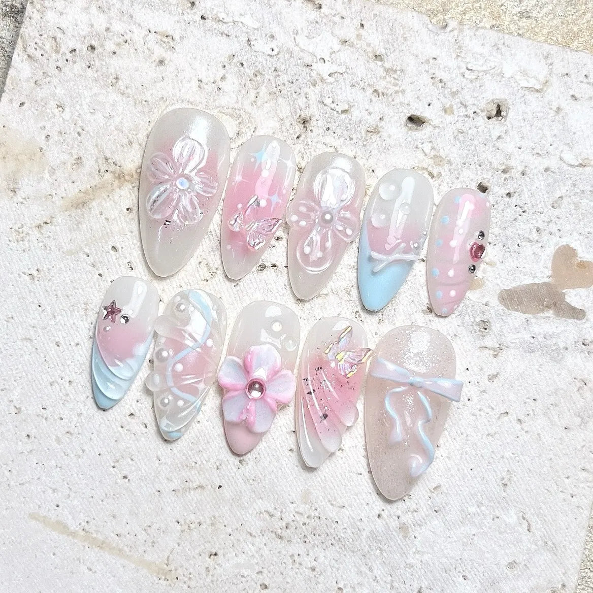 Handmade pastel press-on nails with butterfly, flower, bow, and pearl designs in pink and blue.