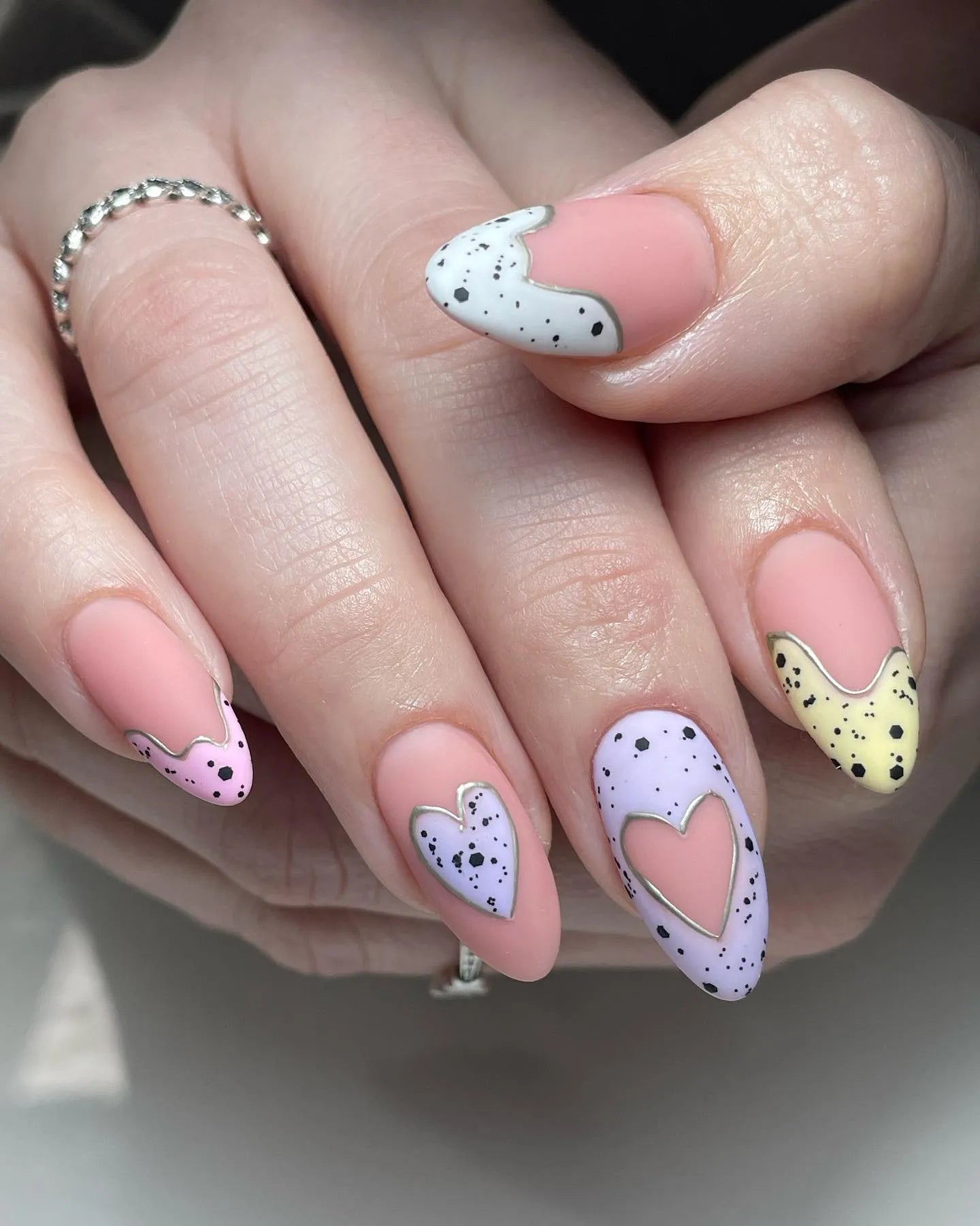 Hand with handmade pastel speckled heart press-on nails in spring colors and silver outline.