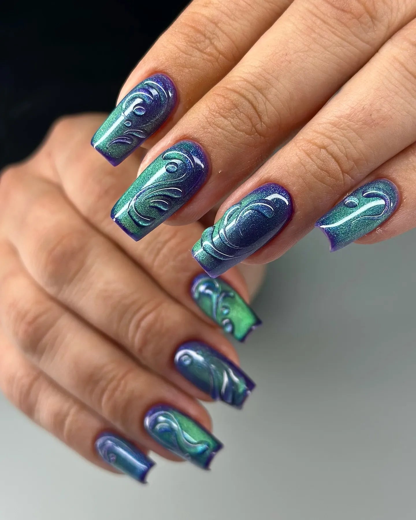 Hand with green and purple 3D swirl press-on nails, glossy and handmade design.