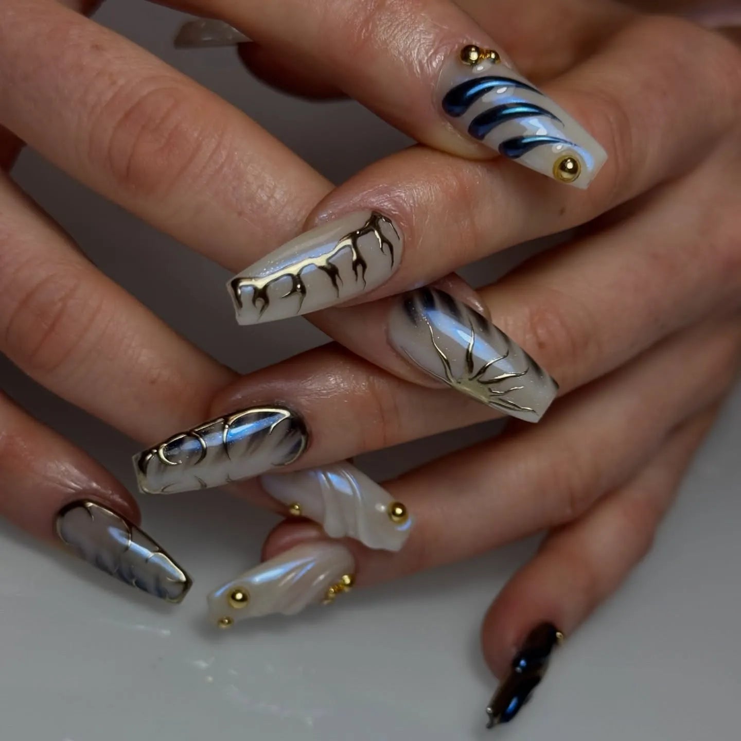 Hand with long handmade pearl white press-on nails, 3D swirl and gold stud accents, modern design