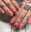 Hand with pink ombre press-on nails featuring gold starburst and sacred heart designs