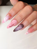 Hand with long almond-shaped press-on nails in pink and brown, featuring 3D bow, lace, and polka dot designs.