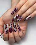 Hand with long press-on nails featuring pink butterfly and floral designs with rhinestones.
