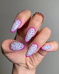 Hand with almond-shaped press-on nails, pink dragon fruit polka dot design, summer nail art