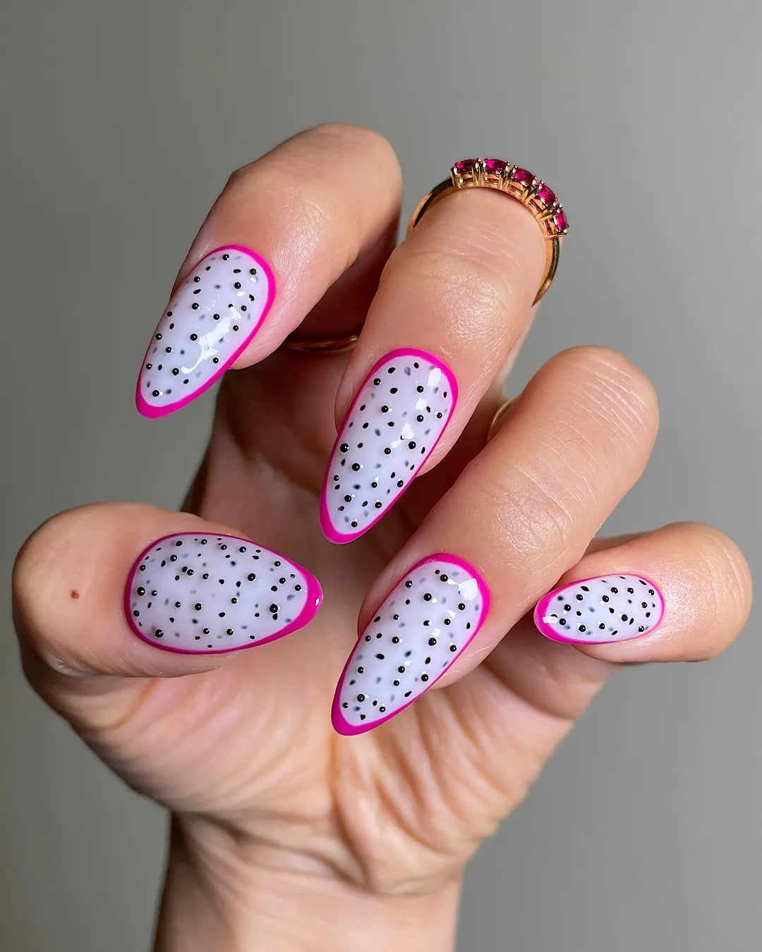 Hand with almond-shaped press-on nails, pink dragon fruit polka dot design, summer nail art