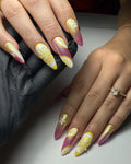 Hand with long press-on nails in pink, gold, and yellow lemonade shimmer with citrus and floral art.