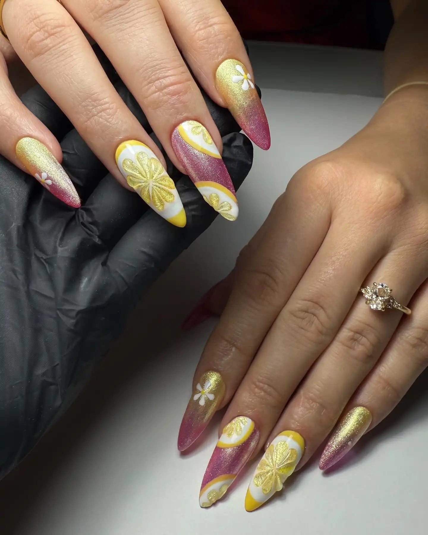Hand with long press-on nails in pink, gold, and yellow lemonade shimmer with citrus and floral art.
