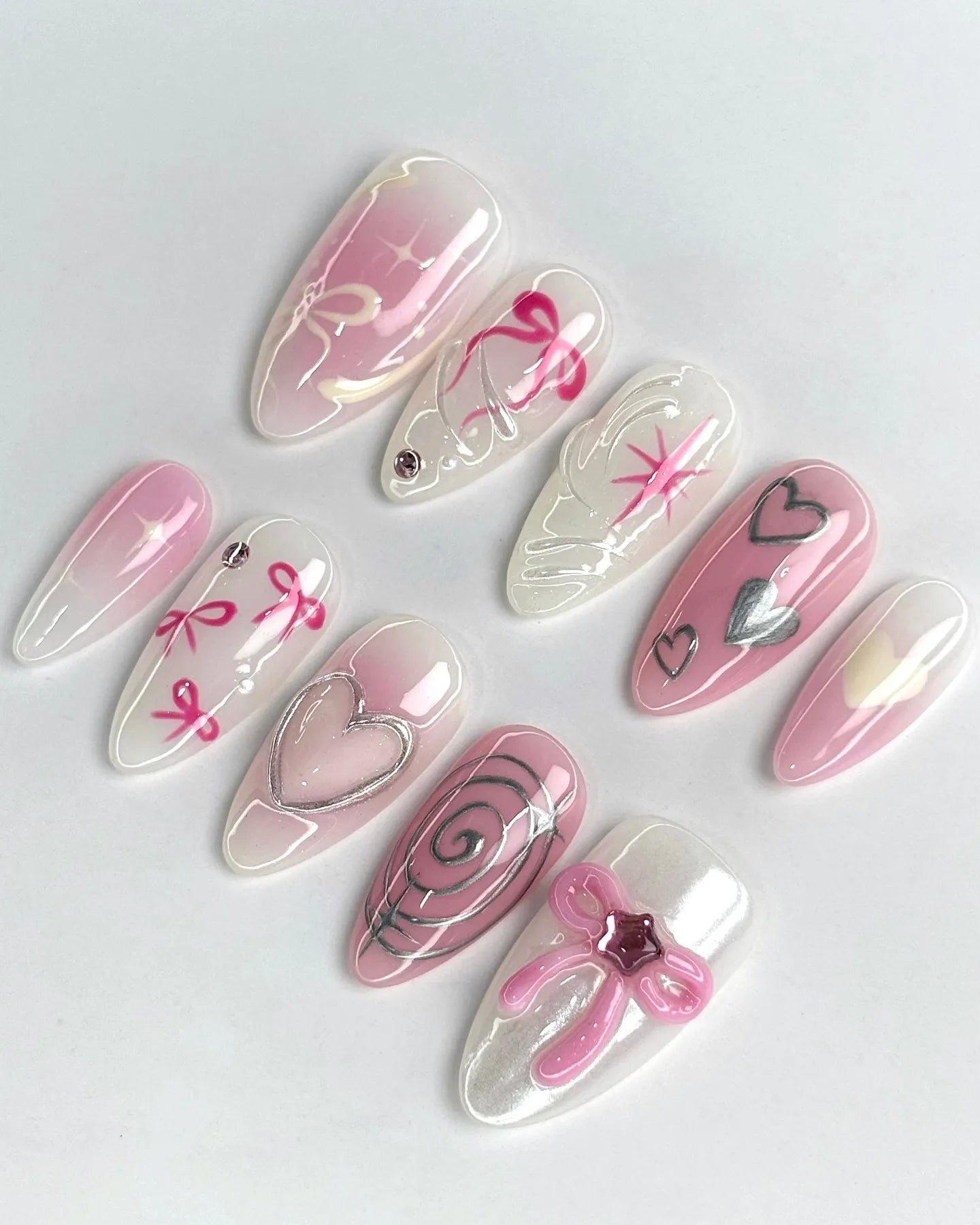 Handmade pink ombre press-on nails with silver hearts, bows, and swirl designs
