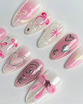 Handmade pink ombre press-on nails with metallic silver hearts, bows, and coquette nail art.