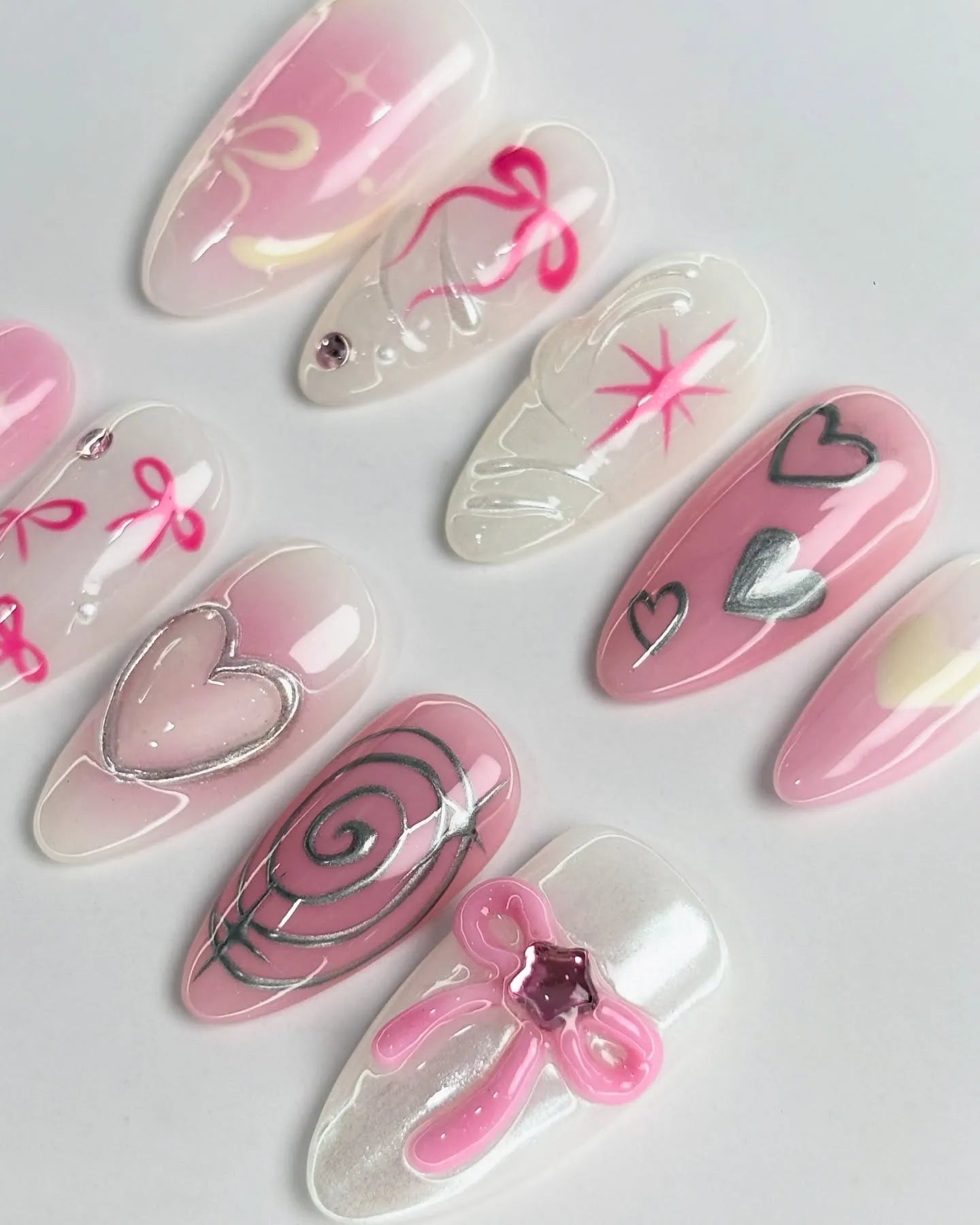 Handmade pink ombre press-on nails with metallic silver hearts, bows, and coquette nail art.
