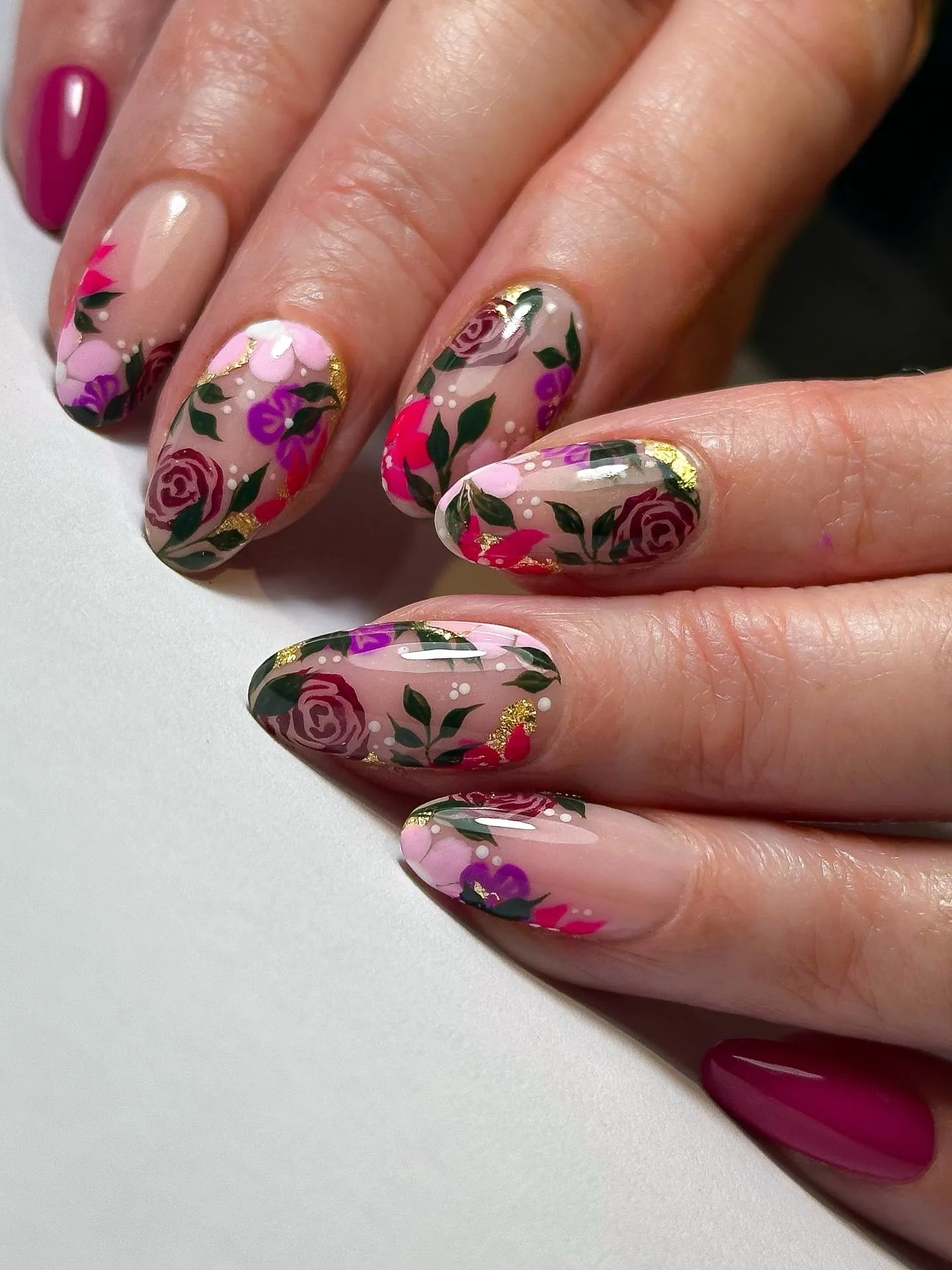 Hand with pink and purple floral rose gold foil press-on nails, garden-inspired nail art.