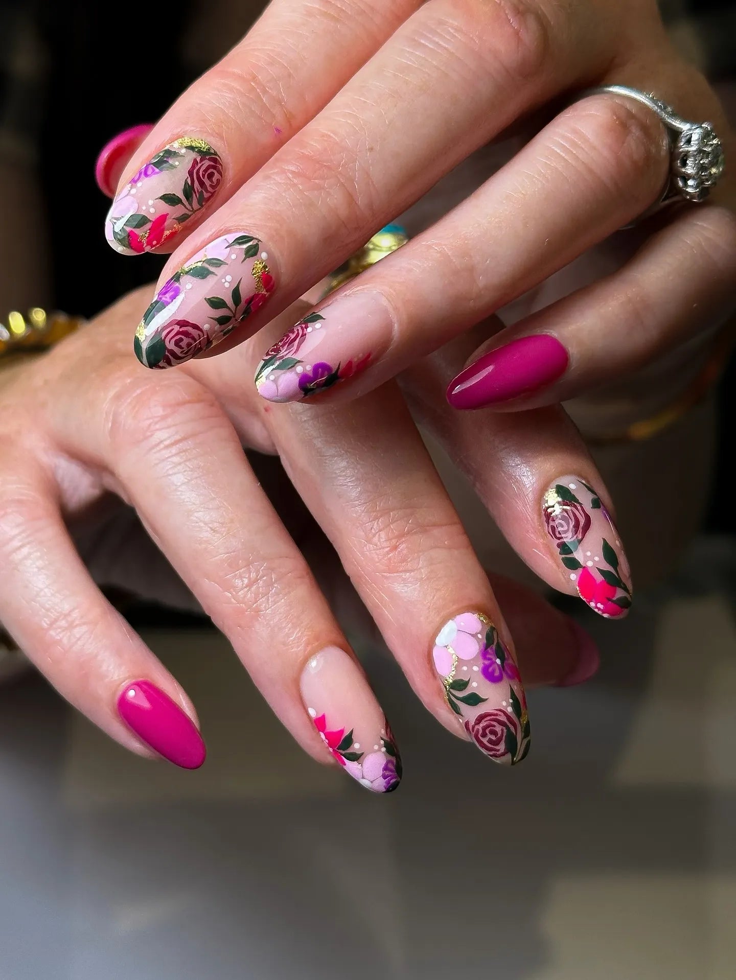 Hand with handmade pink and purple floral press-on nails, rose gold foil accents, garden design.