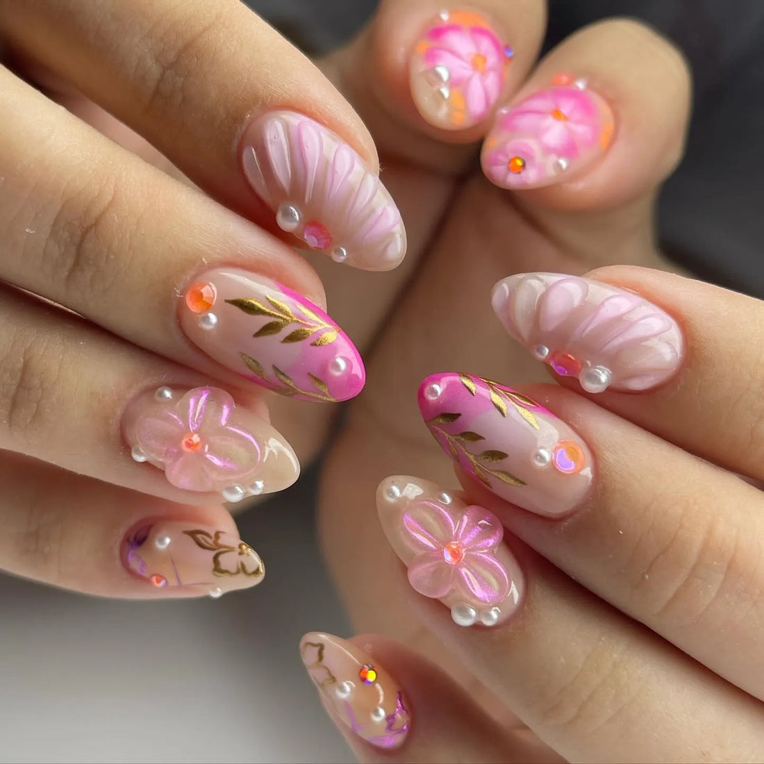 Handmade press-on nails with pink floral designs, gold leaf, pearls, and shell accents.