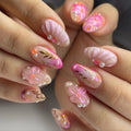 Handmade press-on nails with pink floral designs, gold leaf, pearls, and shell accents.