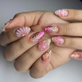 Handmade pink press-on nails with floral designs, gold leaf accents, and pearl embellishments.