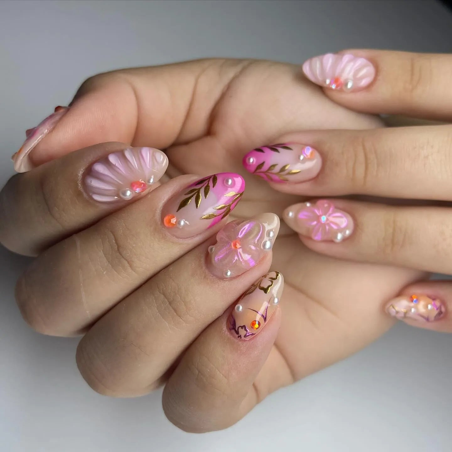 Handmade pink press-on nails with floral designs, gold leaf accents, and pearl embellishments.