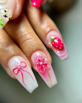 Hand holding long square press-on nails with 3D pink flower, strawberry, and bow designs.