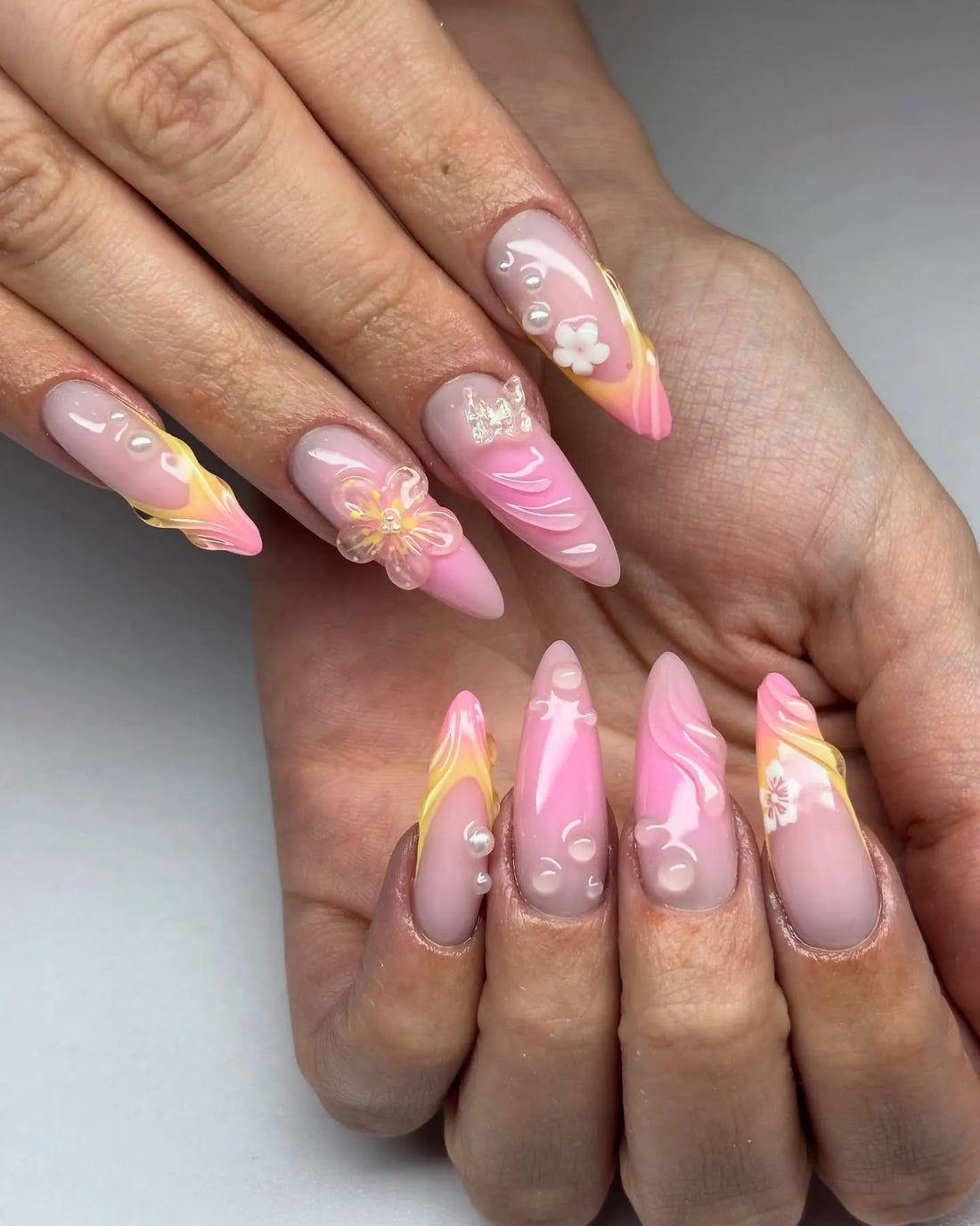 Handmade pink ombre press-on nails with 3D swirl, flower accents, and pearl details