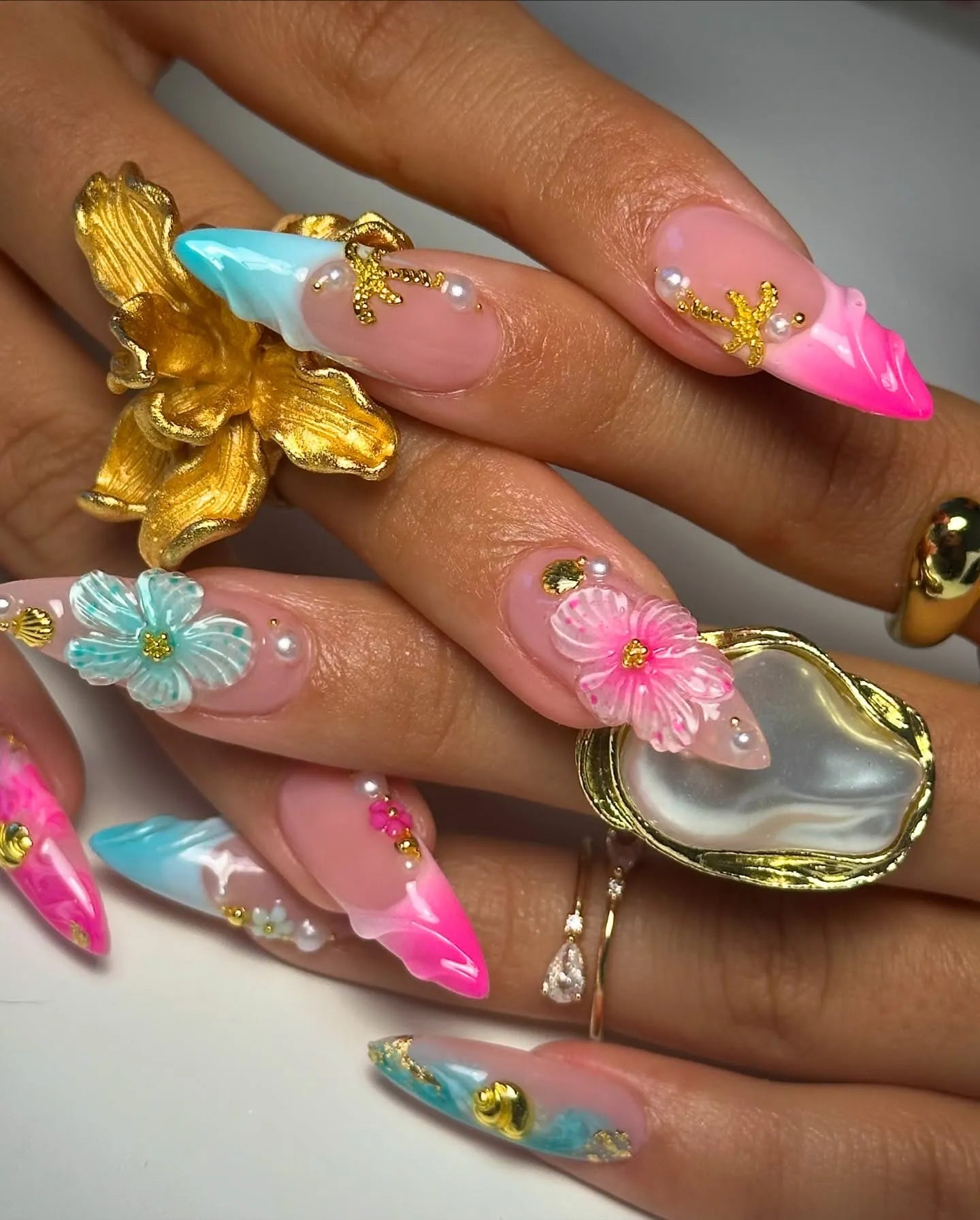 Handmade press-on nails with pink and teal ombre, 3D floral designs, seashell, and pearl accents.