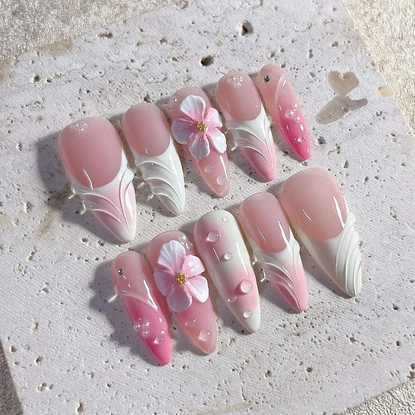 Handmade press-on nails with pink and white ombre, 3D floral accents, and water drop gems.