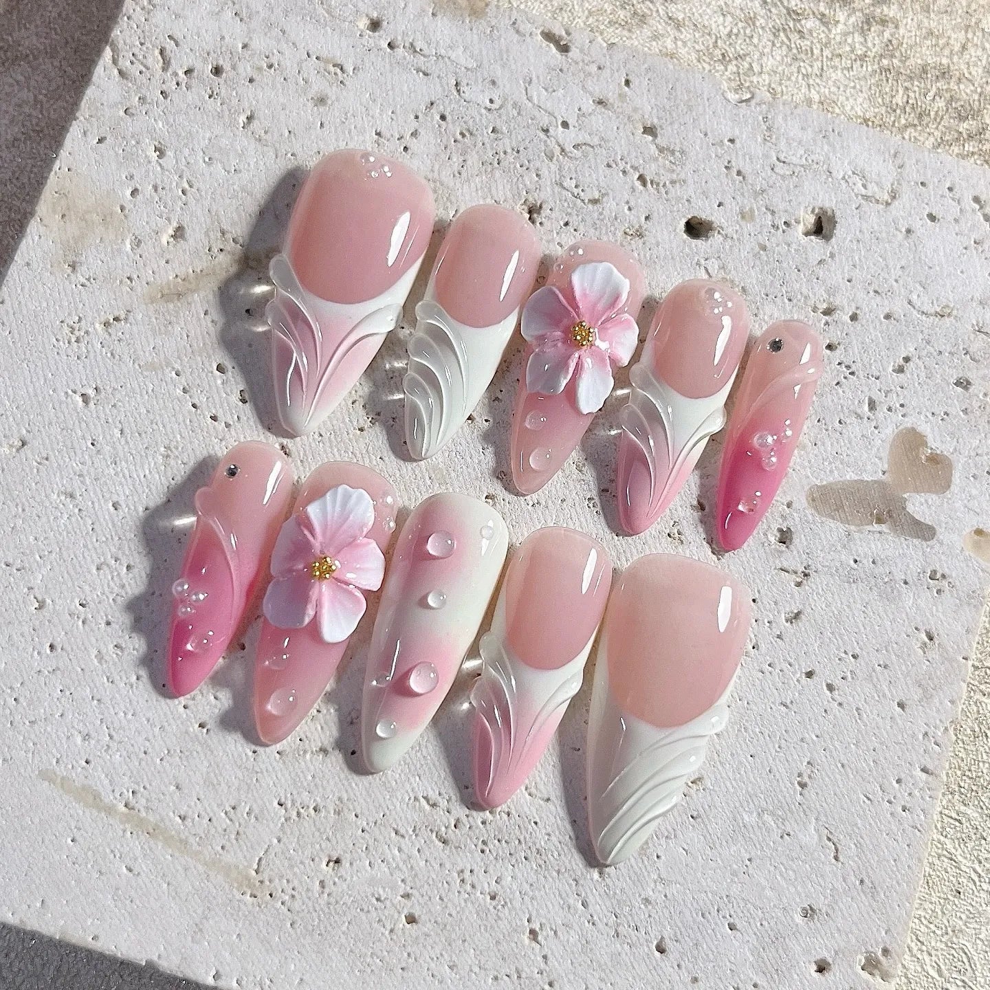 Handmade pink and white 3D floral ombre press-on nails with water drop gems on display