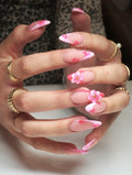 Hand with long press-on nails featuring pink zebra French tips and 3D floral gem accents.
