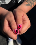 Hand holding pink handmade press-on nails with neon red starburst and black zebra rose art