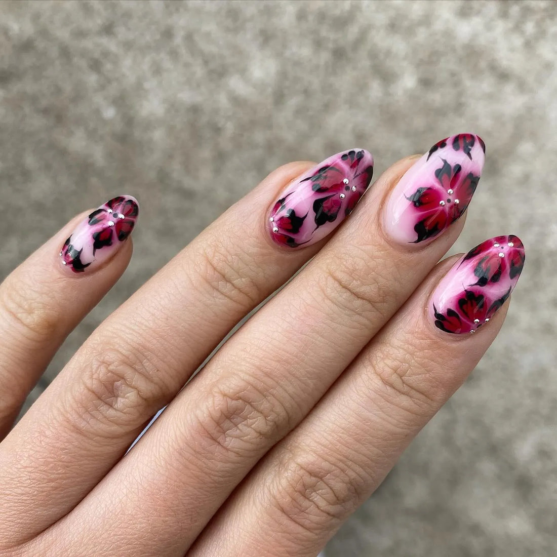 Hand with handmade pink press-on nails featuring red leopard floral artistic design.
