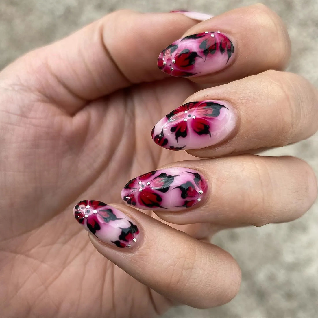 Hand with handmade pink press-on nails featuring red leopard floral artistic design.