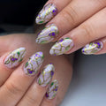 Handmade press-on nails featuring purple floral stained glass design with gold foil accents.