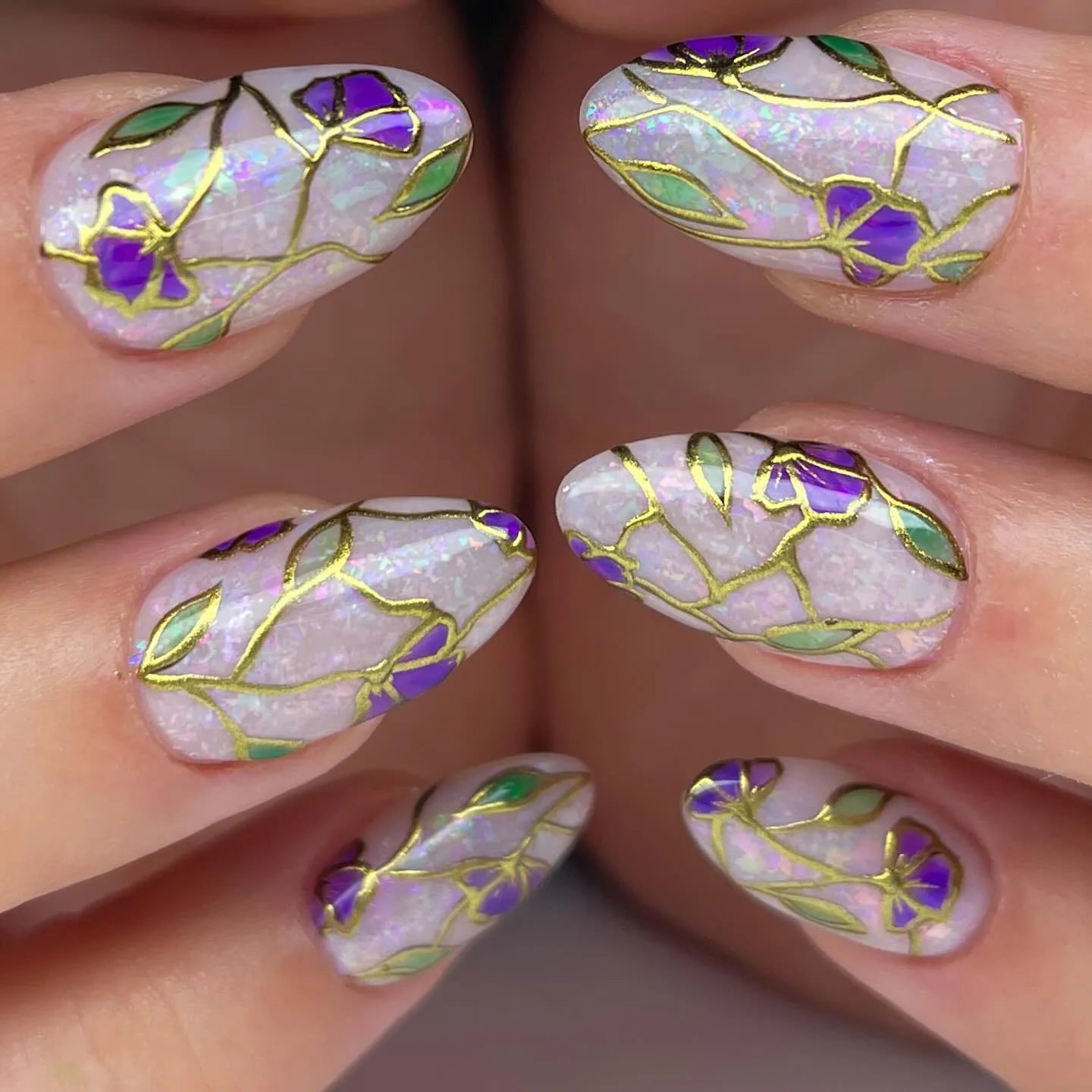Handmade press-on nails with iridescent base, purple floral designs, and gold foil accents.