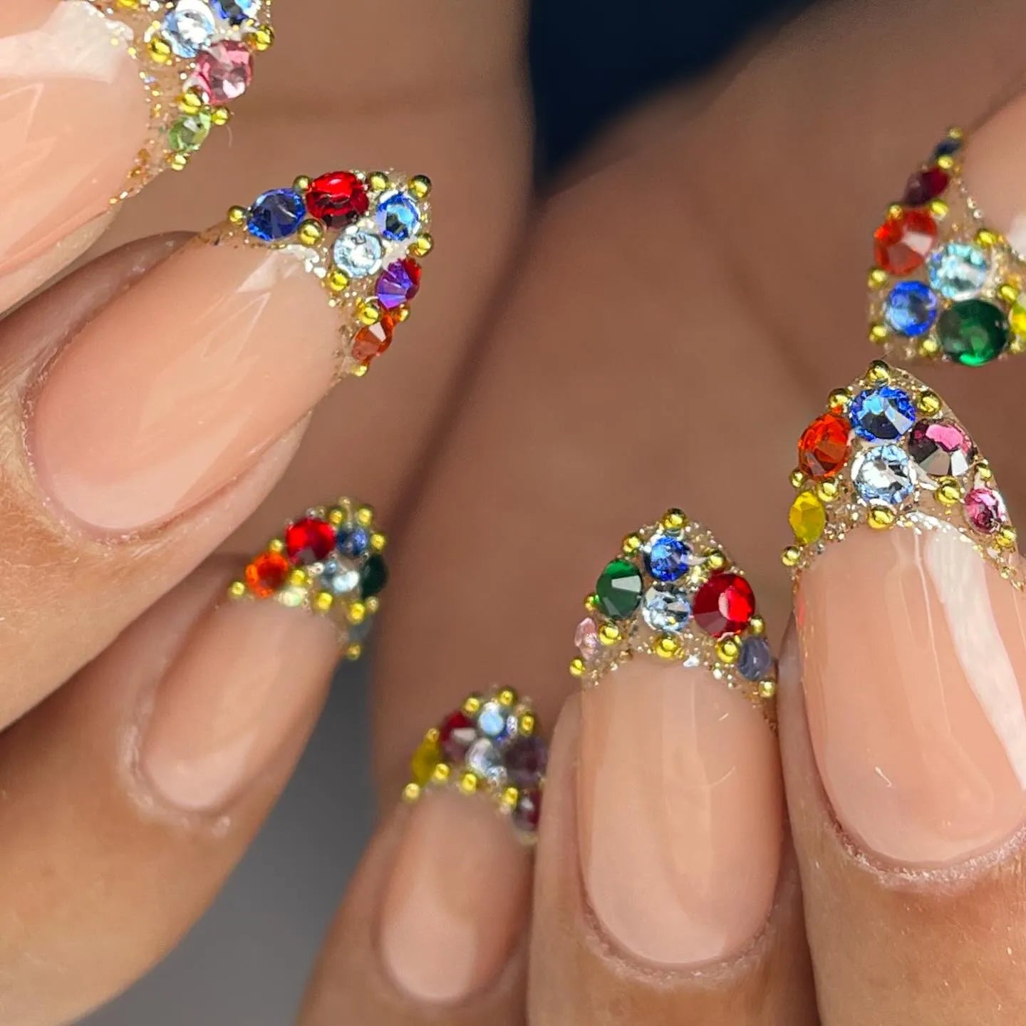 Handmade nude press-on nails with rainbow crystal French tips and gold bead accents.