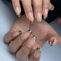 Hand with nude French tip press-on nails decorated with colorful rainbow crystal jewels.