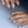 Hand with nude press-on nails featuring rainbow crystal French tip design